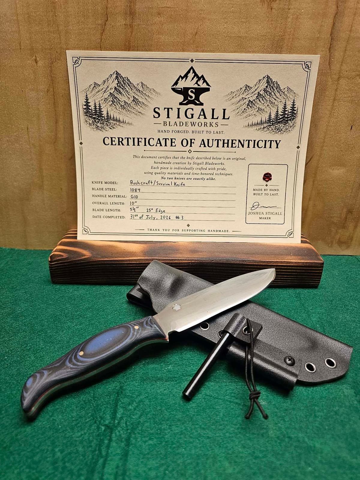 Bushcraft knife with a blue and black G10 handle on a Kydex sheath with a ferro rod, in front of its signed certificate of authenticity
