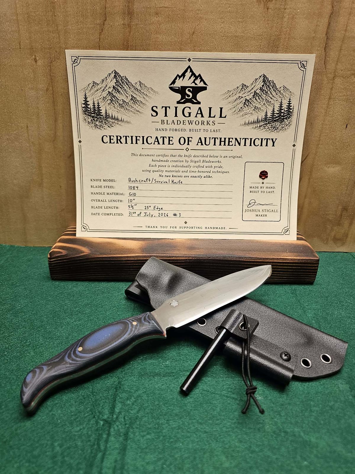 Bushcraft knife with a blue and black G10 handle on a Kydex sheath with a ferro rod, in front of its signed certificate of authenticity