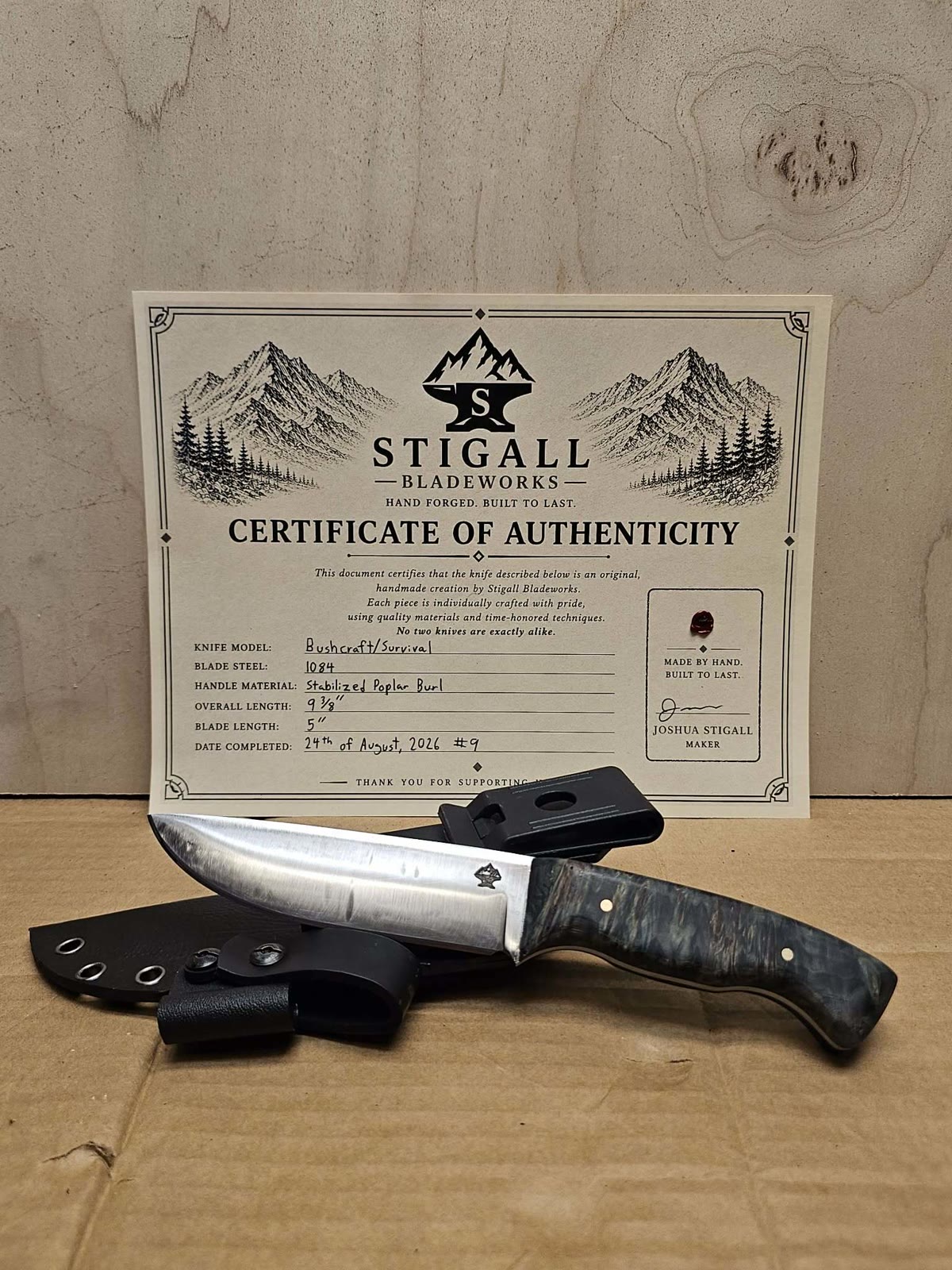 Bushcraft knife with a dark stabilized poplar burl handle and a Kydex sheath with belt clip, in front of its signed certificate of authenticity